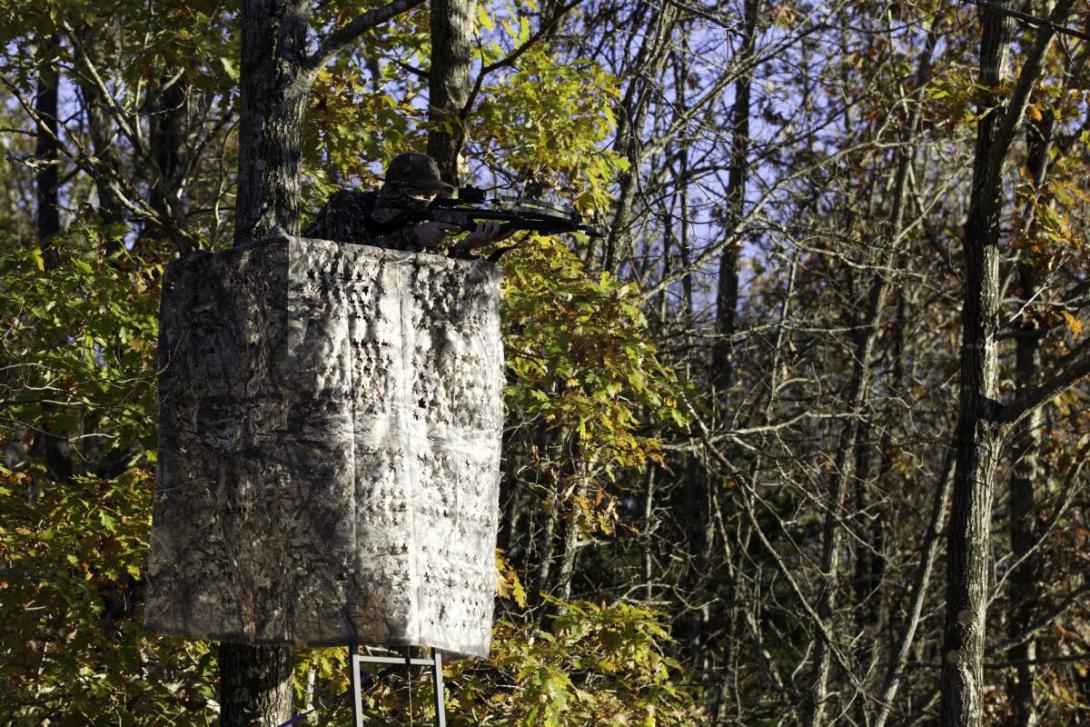 A hunter aims a crossbow from a deer stand