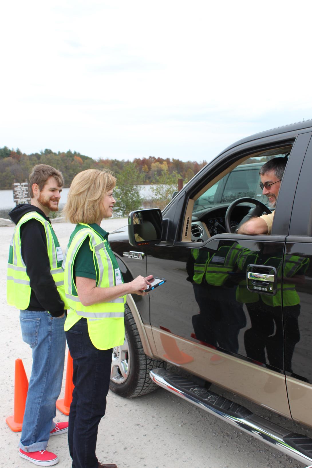 Two staffers in reflective safety vests interview a man in a black pickup truck.