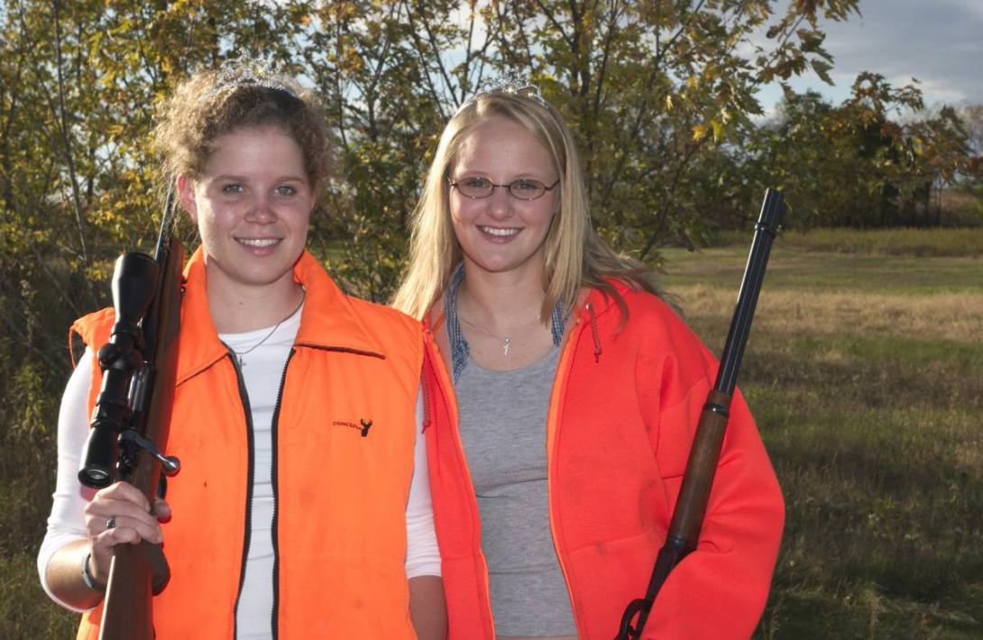 Two women in hunter orange clothing pose with their deer rifles